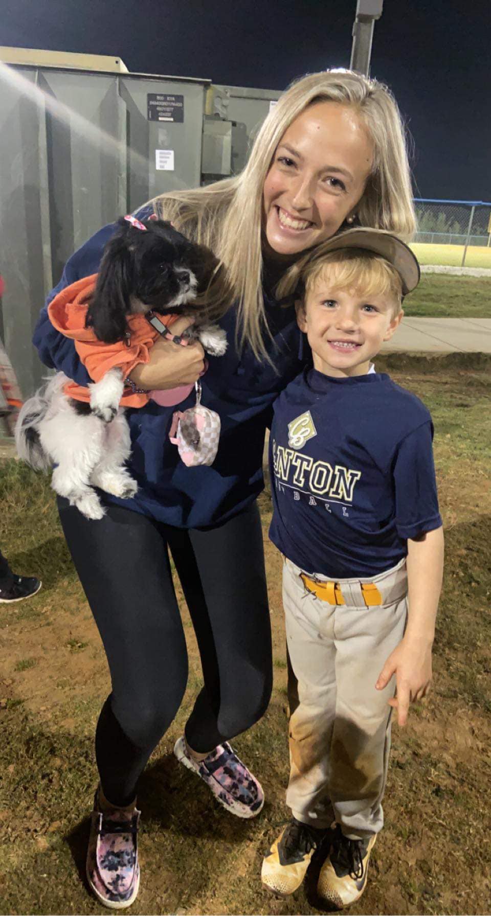 Bree at a ball field holding her dog and standing with a young ballplayer